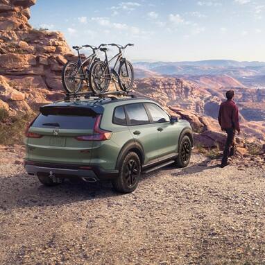 2027 Honda CR-V TrailSport Hybrid in Ash Green Metallic back desert canyon with bikes on roof (Compact Crossover SUV).